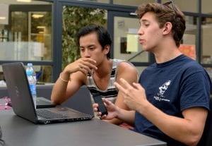Two male students discuss a video they are viewing on a laptop.