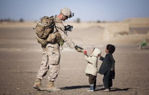 soldier handing something to two little kids