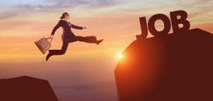A woman wearing a formal business suit and carrying a work bag is jumping from one rock to another rock that is holding up letters that spell "job."