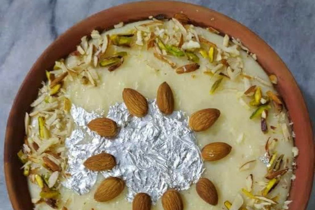 A bowl of kheer with a ring of whole almonds in the middle and chopped pistachios and almonds around the outer edge.