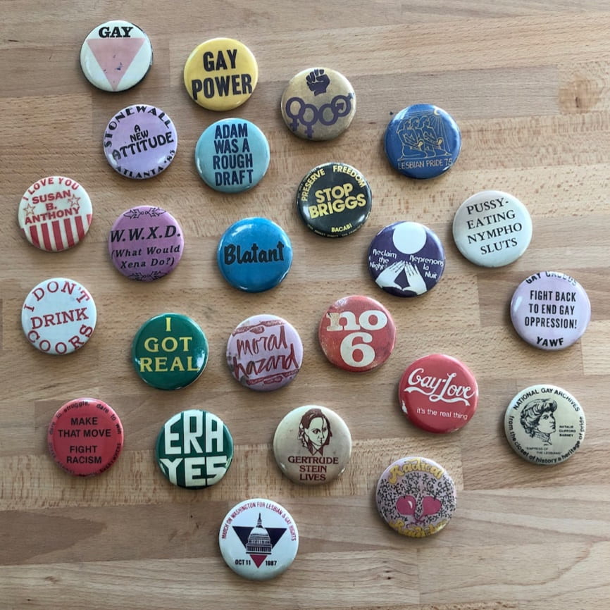 pin-on wearable buttons on a table. the buttons show slogans and icons from queer history in Atlanta