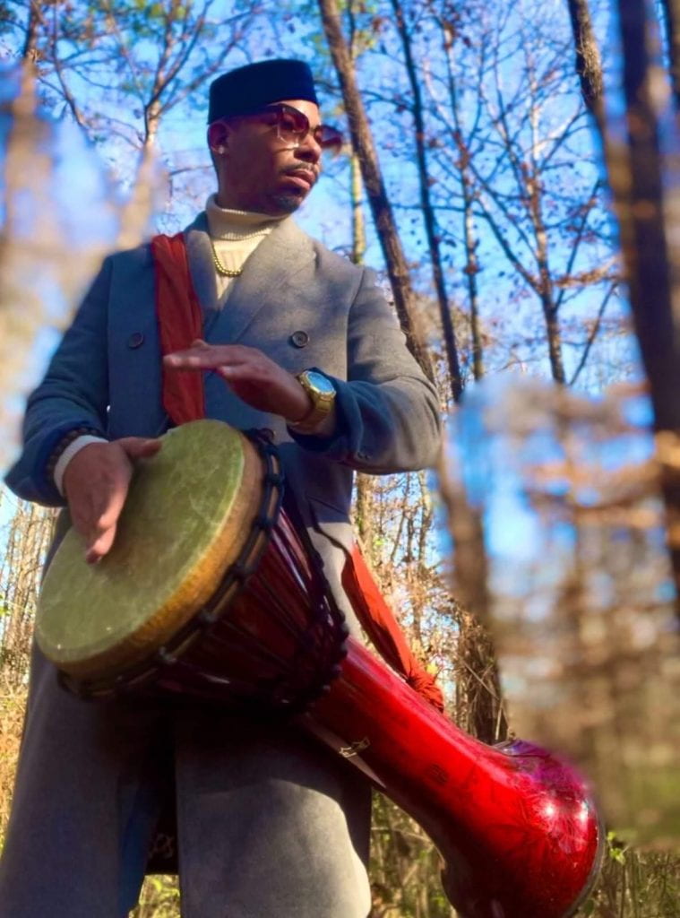 Doctor Calico standing in a forest playing a drum.